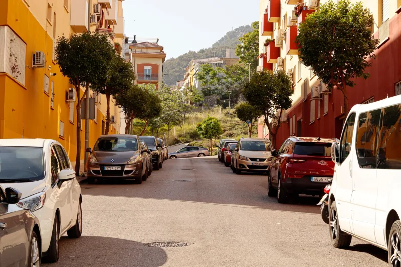 Zonnige stadsstraat met kleurrijke gebouwen en geparkeerde auto's, die een Mediterrane sfeer biedt.