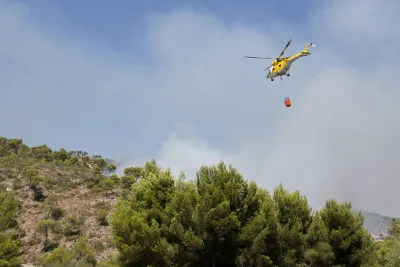 Een helicopter bestrijdt een bosbrand in Spanje en laat water vallen op het brandende gebied.
