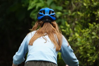 Een persoon in blauwe kleding en een helm fiets in de open lucht in een groen bosgebied.