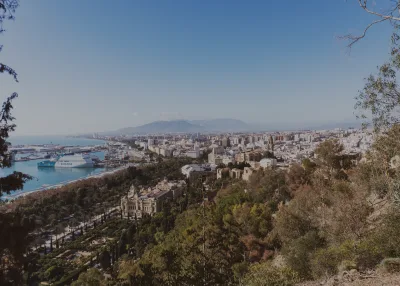 Indrukwekkend vogelperspectief van het stadsgezicht van Málaga met haven en weelderig groen onder een heldere blauwe lucht.