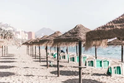 Een serene zandstrand met rieten parasols en een blauwe lucht, perfect voor een zomervakantie in Malaga, Spanje.